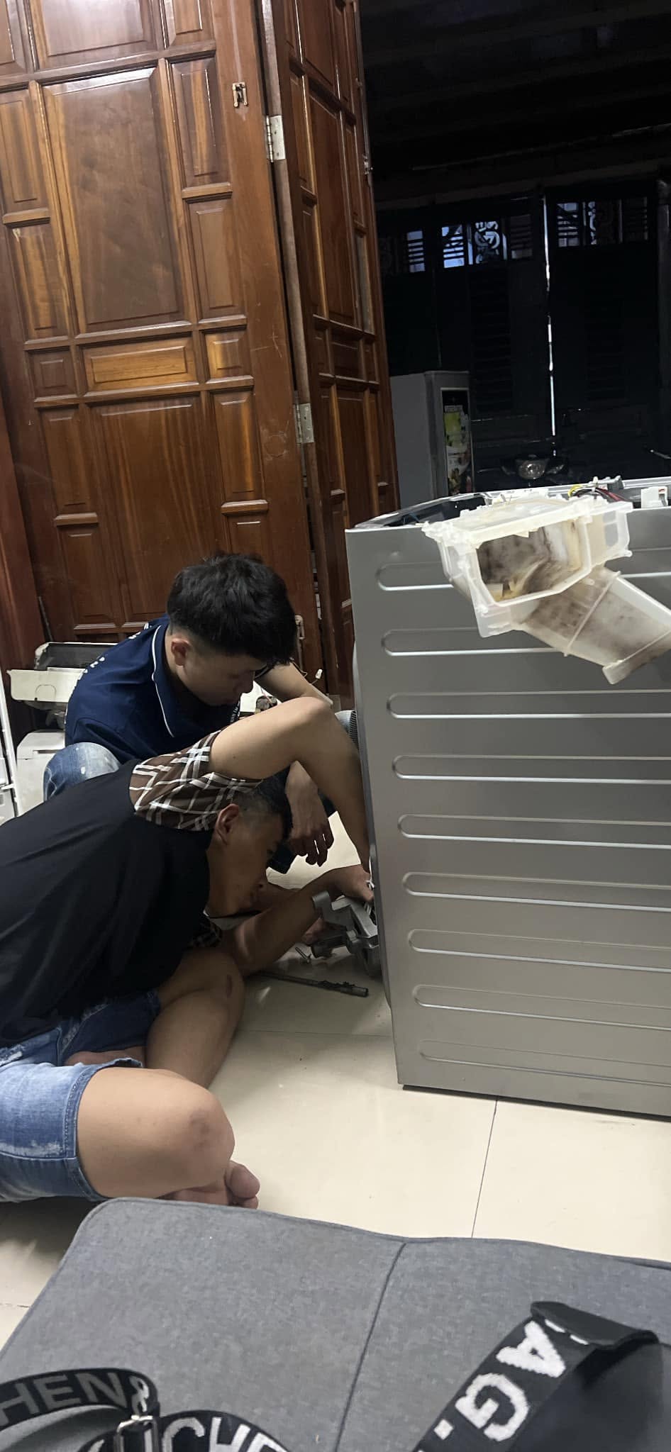 Hai thợ tháo bơm xả phía dưới khi sửa máy giặt quận 10 tại nhà khách