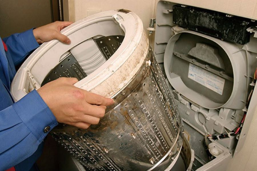 Thợ nhấc lồng giặt bám cặn ra khỏi máy giặt cửa trên để vệ sinh