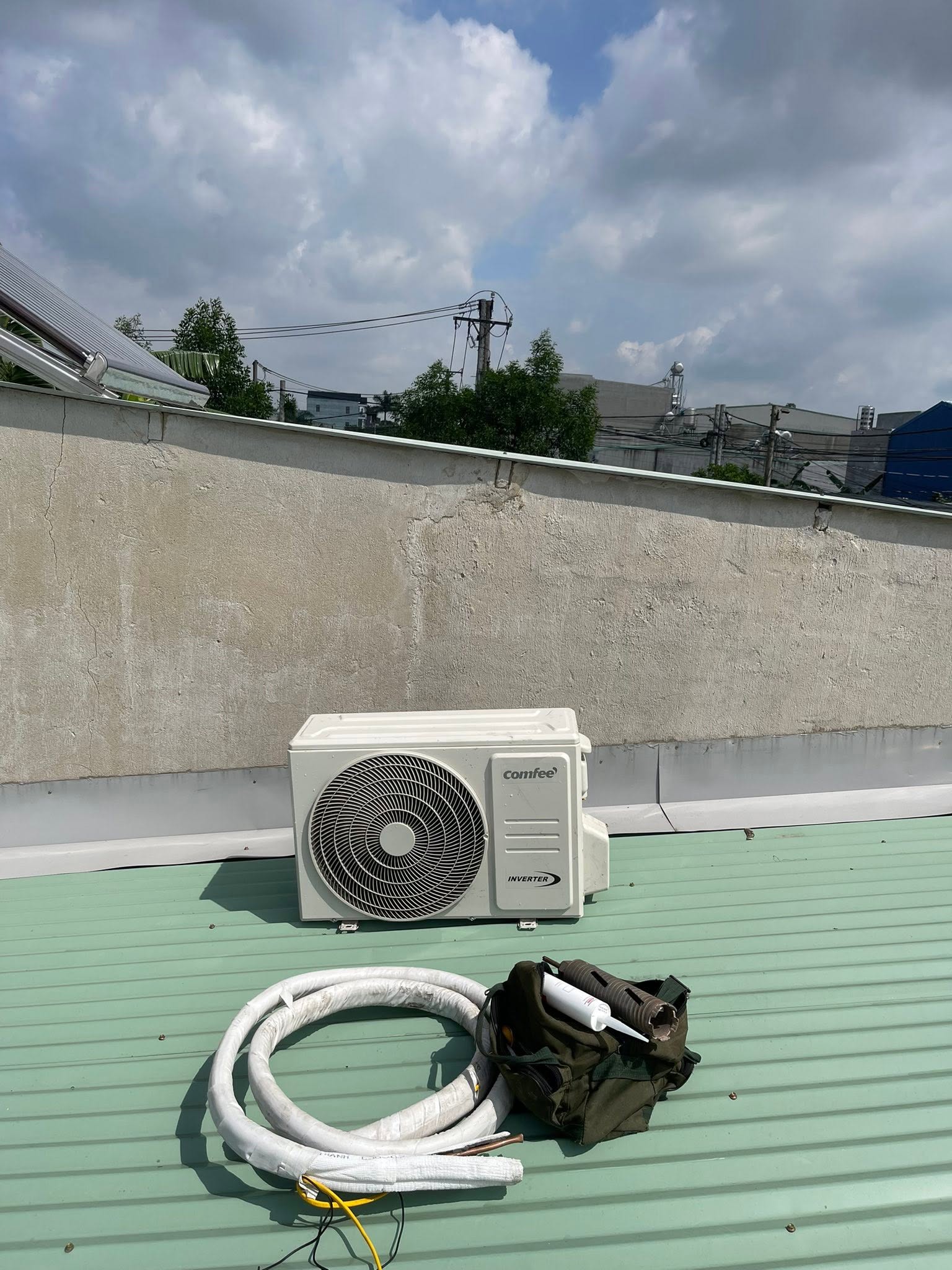 Dàn nóng máy lạnh Comfee inverter đặt trên mái tôn cạnh cuộn ống đồng và túi đồ nghề của thợ