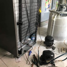 Lưng tủ lạnh lộ dàn nóng, block cũ tháo ra đặt cạnh dụng cụ khi sửa tủ lạnh bình tân