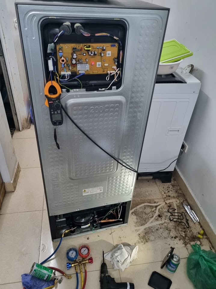 Bo mạch sau lưng tủ mở nắp, ampe kìm và đồng hồ gas đặt cạnh khi sửa tủ lạnh quận 4