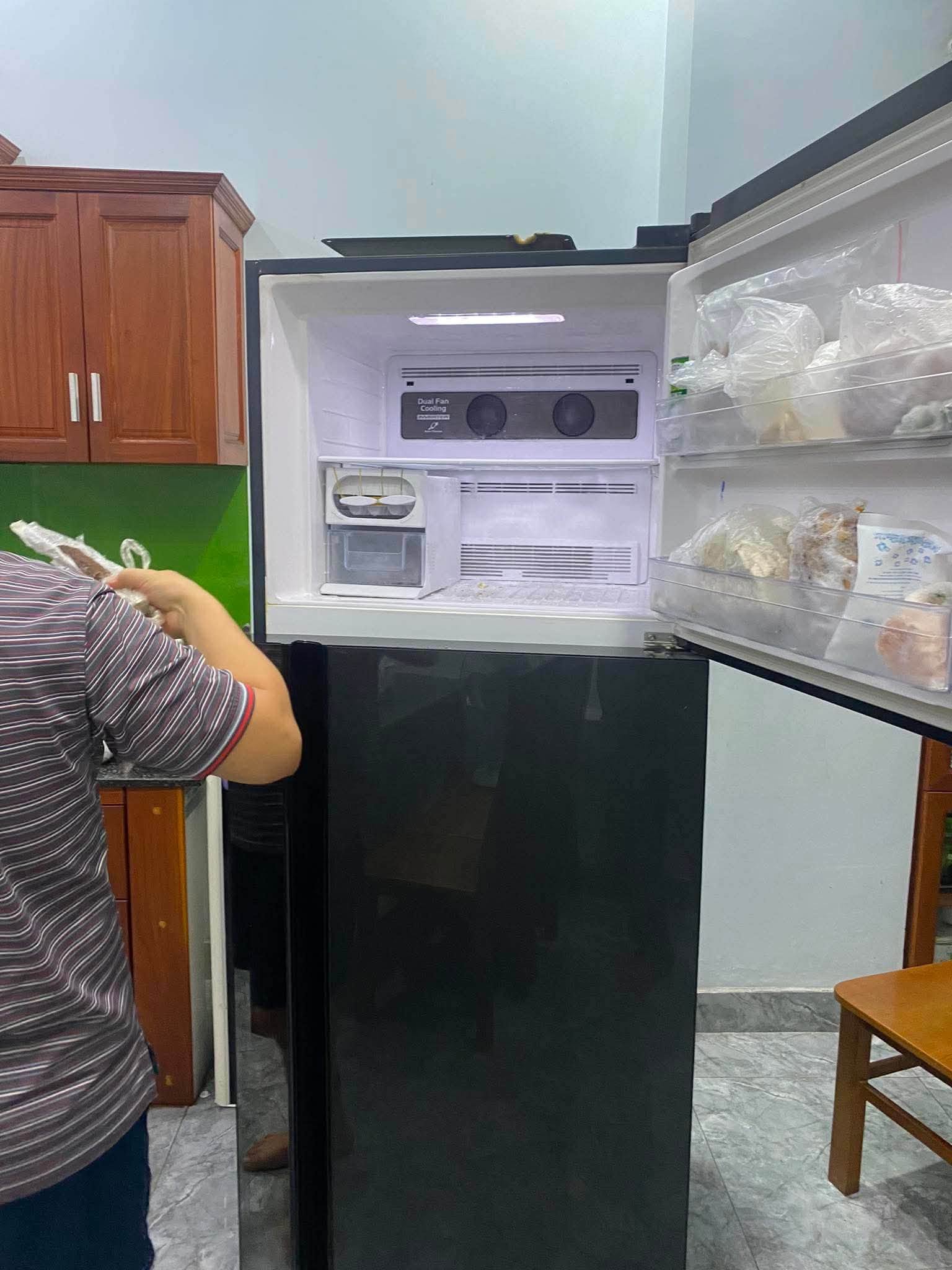 Người mở ngăn đông tủ lạnh màu đen, bên cạnh là tủ bếp gỗ