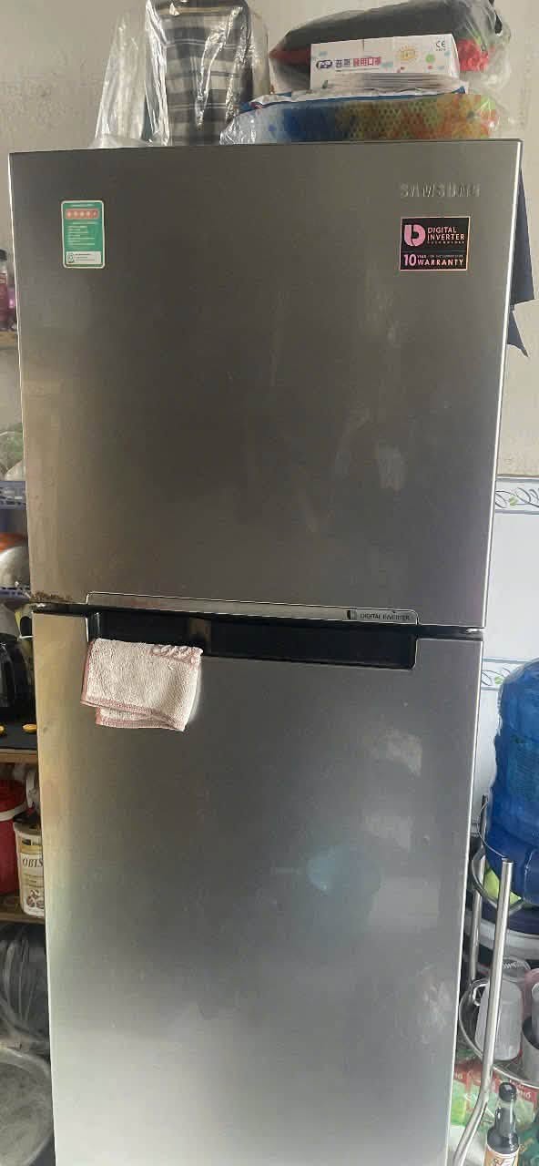 Tủ lạnh 2 cánh inverter màu bạc, khăn lau treo ở tay nắm, kê sát kệ đồ trong bếp