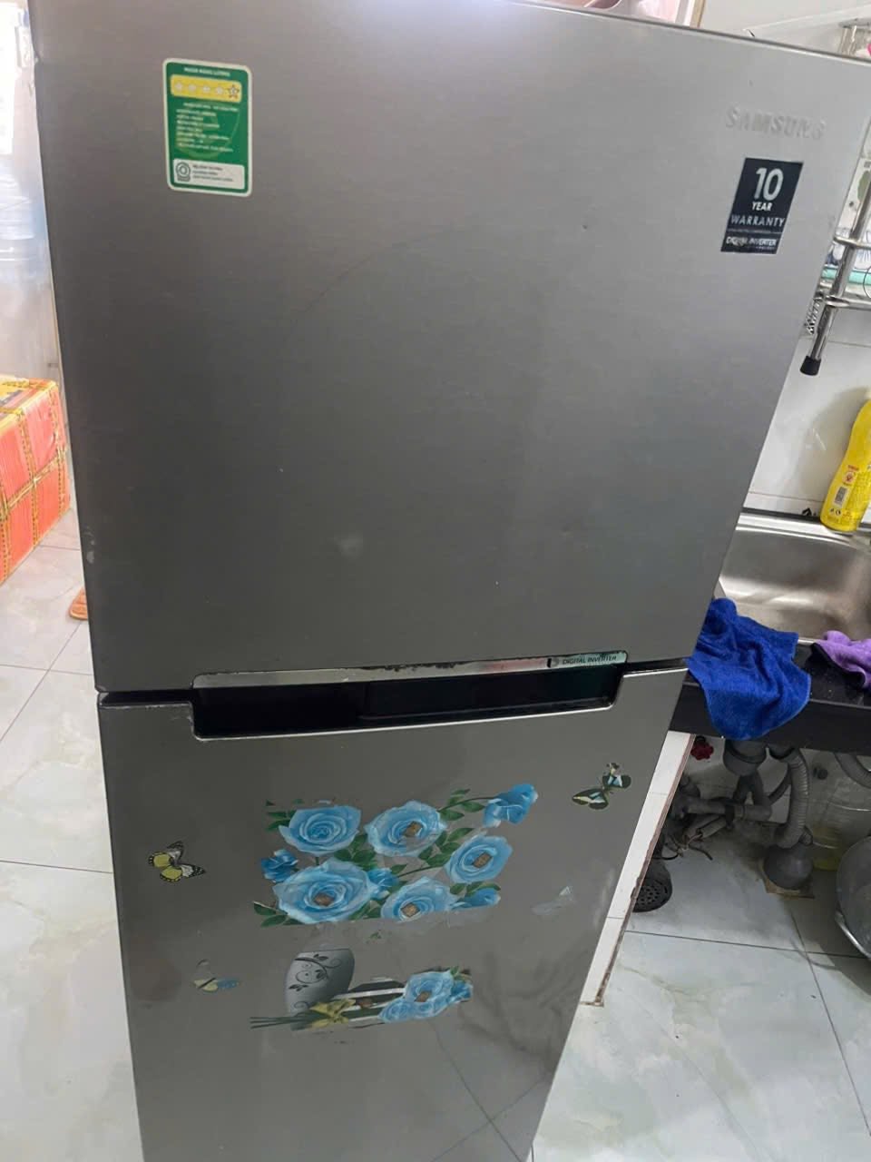 Tủ lạnh 2 cánh inverter màu bạc dán hình hoa, kê trong bếp cạnh bồn rửa chén