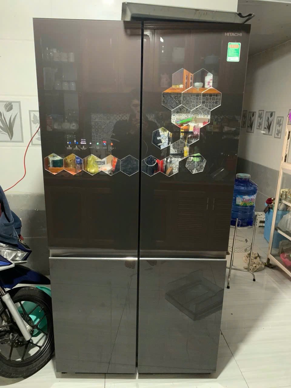 Tủ lạnh nhiều cánh mặt kính nâu dán miếng trang trí lục giác, đặt trong nhà cạnh xe máy