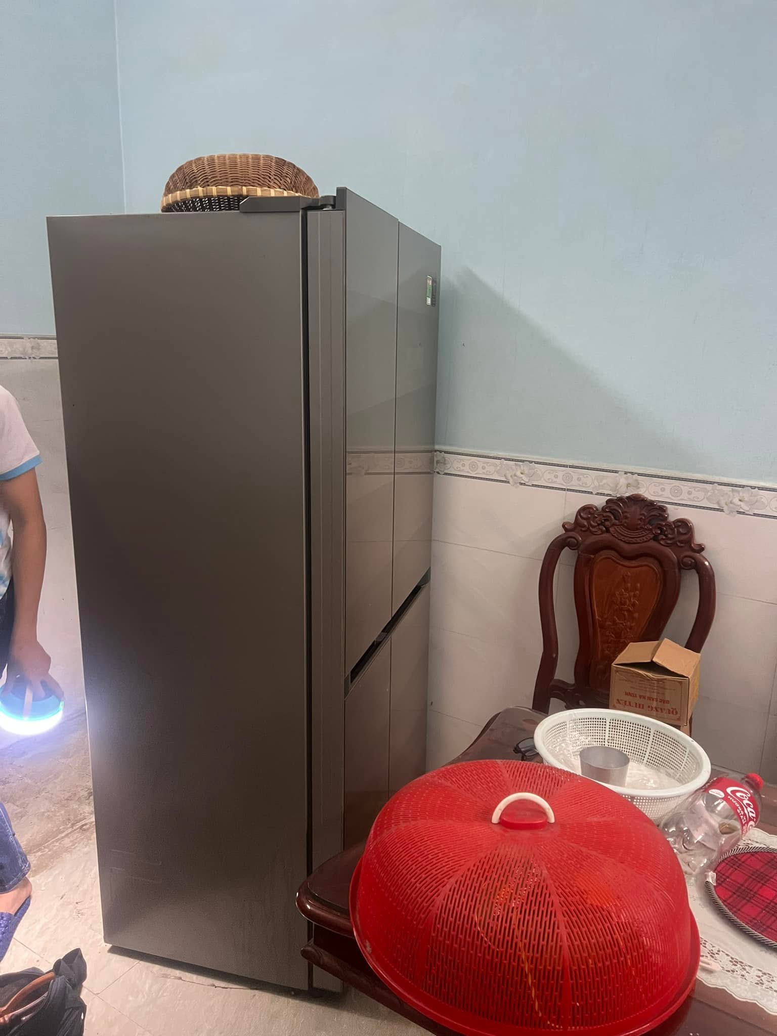 Tủ lạnh nhiều cánh màu xám kê sát tường, người cầm đèn đứng bên cạnh
